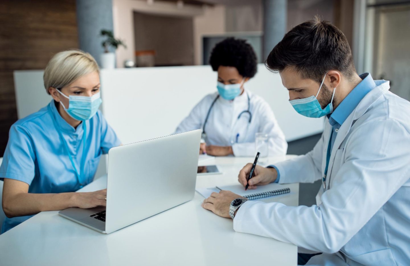 male-doctor-taking-notes-while-working-with-colleagues-medical-clinic